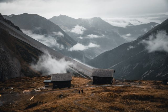 Berglandschaft mit Hütten und ziehenden Wolken.